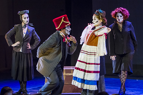 Four actors with expressive makeup perform a scene from an opera on stage